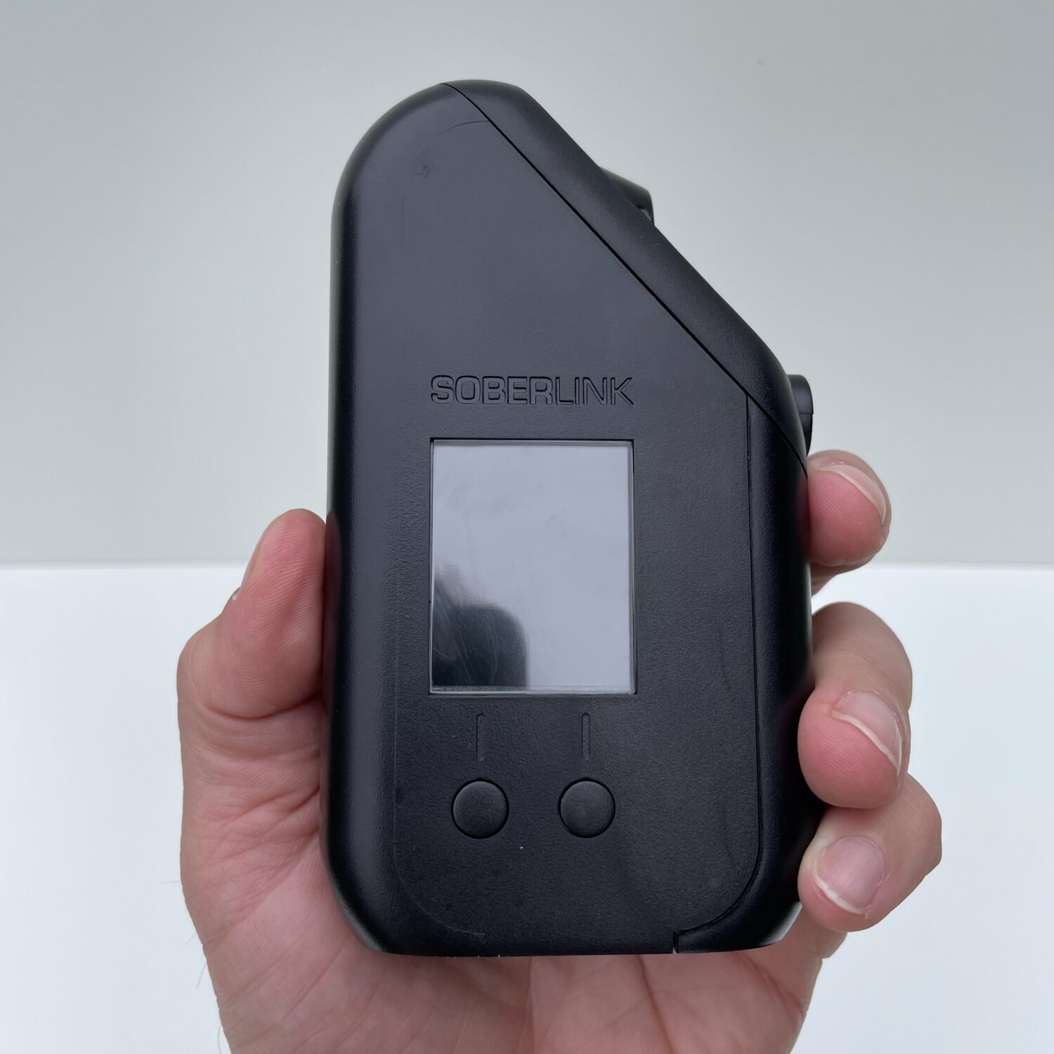 Soberlink Cellular breathalyzer device held in hand showing front display and buttons
